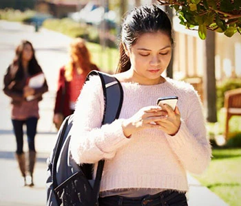 Female student with phone walking on college campus 